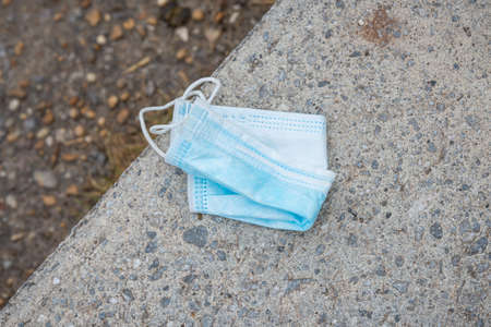 Disposable face mask discarded on concrete floor, pollution linked to the coronavirus pandemic.