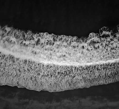 Top down aerial view of sea wave and foam in black and white. Ocean water and beach background with...
