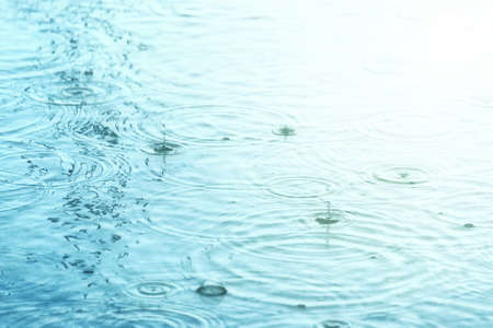 Raindrops creating concentric circles and droplets on a puddle water surfaceの写真素材
