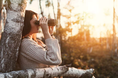 Young woman enjoying outdoors in forest and looking around with binocularsの写真素材