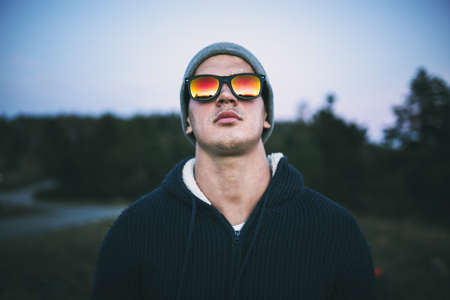 Youn attractive man with sunglasses standing and posing while looking in sunset. Outdoors portrait.の写真素材