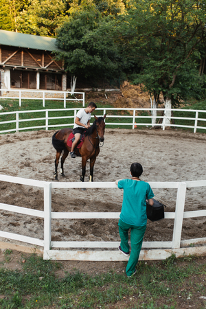 Veterinarian woman standing in front of horse coral and watching at injured and recovering animal with horsemanの写真素材