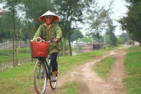 NAM DINH, VIETNAM - MARCH 28, 2010: A woman farmer is biking home from her work on the paddy fieldのeditorial素材