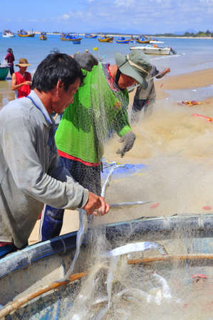 LAGI, VIETNAM - FEBRUARY 26, 2012: Local fishermen are removing fishes from their fishing nets in the Lagi beachのeditorial素材