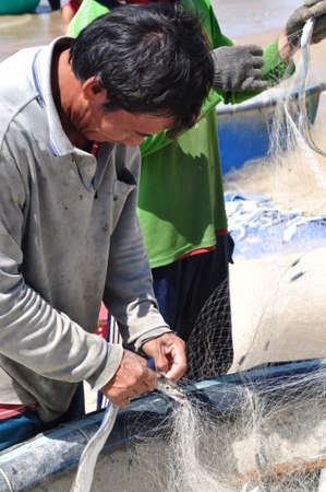 LAGI, VIETNAM - FEBRUARY 26, 2012: Local fishermen are removing fishes from their fishing nets in the Lagi beachのeditorial素材
