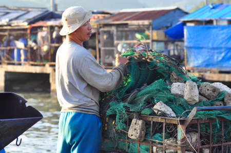 NHA TRANG, VIETNAM - OCTOBER 22, 2011: A fisherman is preparing his fishing net for a new working day at a local seaportのeditorial素材