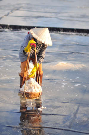 NINH HOA, VIETNAM - MARCH 2, 2012: Vietnamese women are burdening hard to collect salt from the extract fields to the storage fieldsのeditorial素材