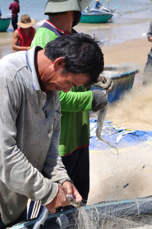 LAGI, VIETNAM - FEBRUARY 26, 2012: Local fishermen are removing fishes from their fishing nets in the Lagi beachのeditorial素材