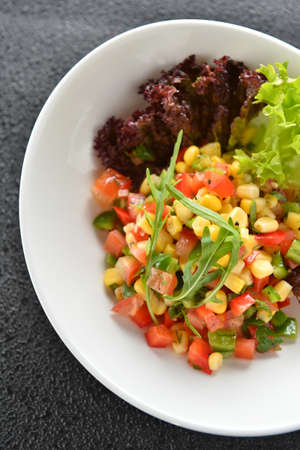Special salad with corn tomato and herbs on white plate in restaurantの写真素材