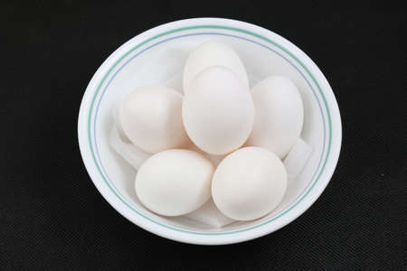 White duck eggs in white bowl in black background