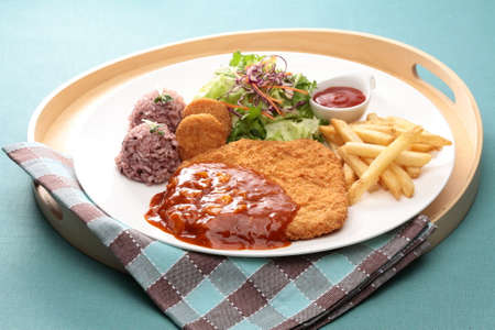Assorted pork cutlet with cripsy potato, rice, salad and chili sauce on wooden trayの写真素材
