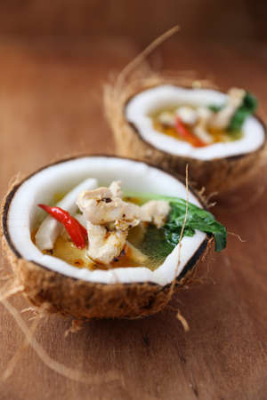 Coconut chicken soup with chili and herbs on wooden table