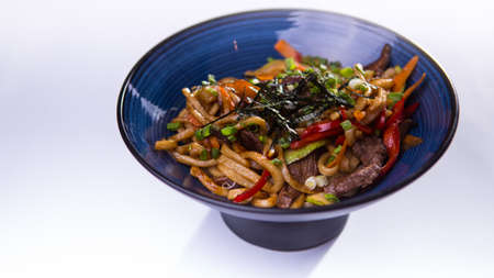 Udon with beef and vegetables in blue chinese bowl on white backgroundの写真素材