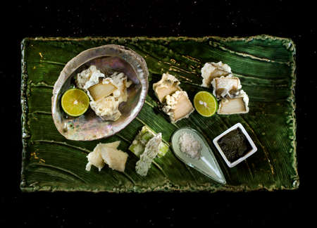 Abalone tempura with black sauce, lemon and salt on wooden tray in black background