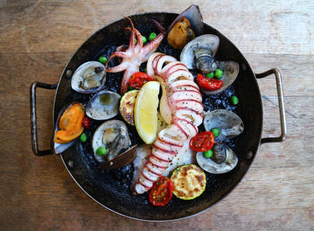Spainish international cuisine orthodox with fried squid, clams, octopus, lemon and mussel in black panの写真素材
