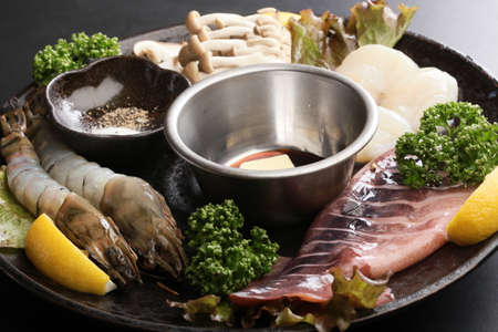 Seafood hot pot with fresh raw shrimp, squid, scallop, lemon, cumin, lettuce and mushroom on big black platterの写真素材
