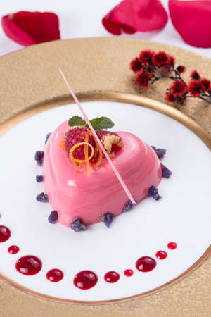 Pink jelly cake in heart shape with red berries and chocolate on white platterの写真素材