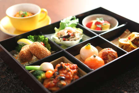 Bento of Temari sushi, shrimp and marinated mushrooms, egg grilled tomato, spring vegetables, beef...