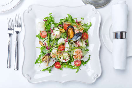 Seafood salad with clams, shrimps, squid, lettuce, tomatoes and herbs on white plateの写真素材