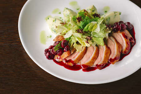 Sliced roasted duck with lettuce, potatoes and sauce on white plateの写真素材