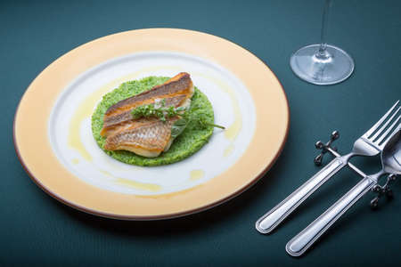 Fried barramundi fish with green vegetables cake on plate in restaurant