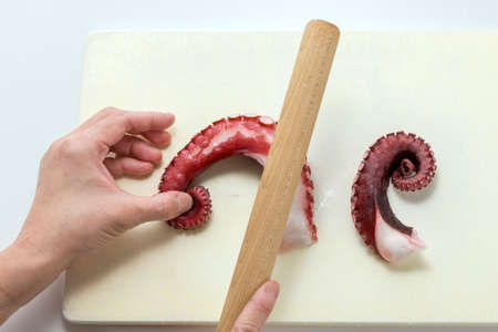 Beating up octopus foot for roasting on wooden cutting board in kitchenの写真素材