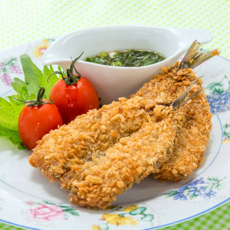 Fried breaded fish tempura with onion sauce and fresh tomatoes on white platterの写真素材