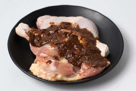 Fresh raw chicken legs seasoned with sauce on black dishの写真素材