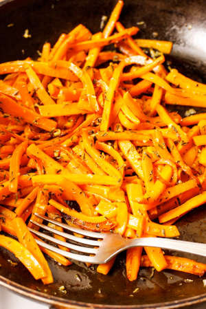 Fried carrots with thyme and garlic on black panの写真素材