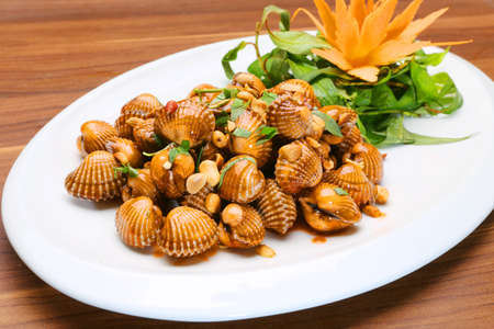 Sauteed blood cockles with peanuts and laksa leaves on white platterの写真素材
