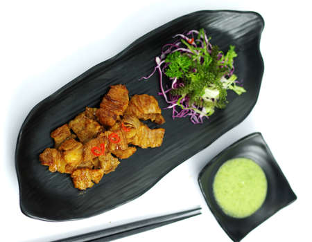 Braised pork with chili sauce and salad on black platterの写真素材