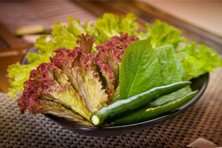 Fresh green chili pepper with lettuce on black bowlの写真素材