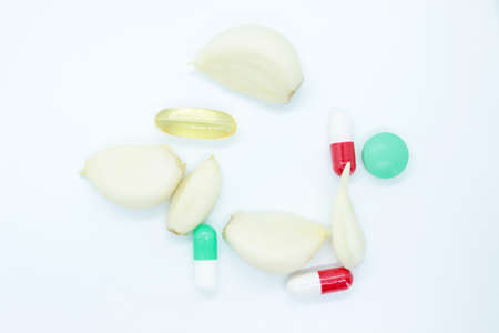 Peeled garlic and vitamins located on a white background