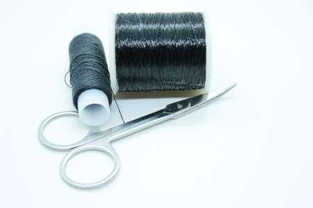 Two spools of black thread and scissors located on a white backgroundの写真素材