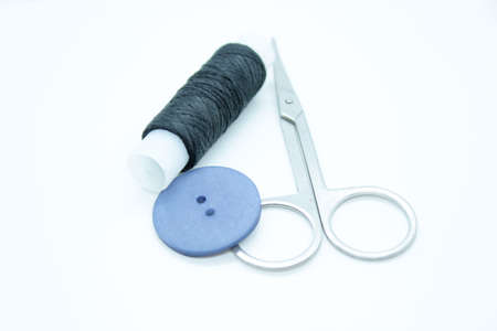 Spool of black thread, a button and scissors located on a white background