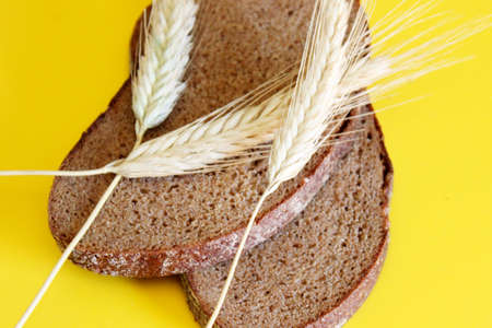 Pieces of sliced rye bread and ripe ears of rye are located on a yellow backgroundの写真素材