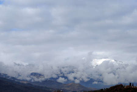 mountain landscapes, winter with clouds covering the high mountains covered with snow at times exposing a small mountain villageの写真素材