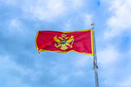 Flag of Montenegro against cloudy sky and windy weather