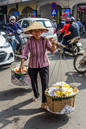 HANOI, VIETNAM - NOVEMBER 13: Vietnamise saleswoman in traditional clothes sales fruits on street at November 13, 2016 in Hanoi, Vietnamのeditorial素材