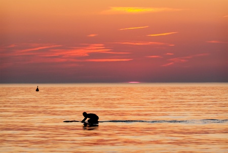 Surfer in the water at sundown against orange sky.の写真素材