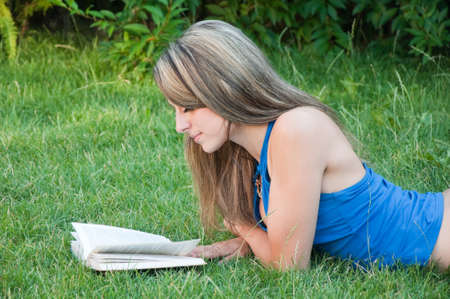 Beautiful girl lies on meadow and reads the book の写真素材