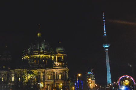 Nighttime photo of the Berlin Cathedral with its illuminated dome, the Fernsehturm TV Tower glowing in blue light, and a Ferris wheel shining in the city skyline of Berlin.の写真素材