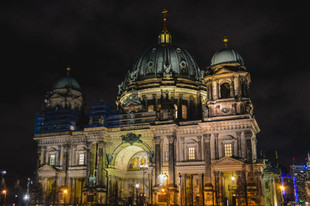 Nighttime photograph of Berlin Cathedral with illuminated dome, ornate facade and sculptures, showing historic German architecture and famous religious landmark in Berlin Germany.の写真素材