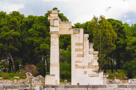 Ancient temple ruins at the Epidaurus archaeological site in Greece, with marble columns and preserved stone walls, set against a natural backdrop of forest trees.の写真素材