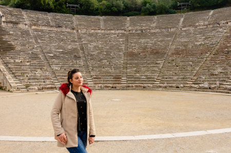 Portrait of a woman in beige coat with red fur detail posing at the center of the Ancient Epidaurus...