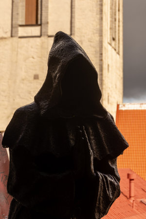 Atmospheric photo of a hooded bronze monk statue in praying stance, with dramatic light and medieval buildings in the old town of Tallinn, Estonia.の写真素材