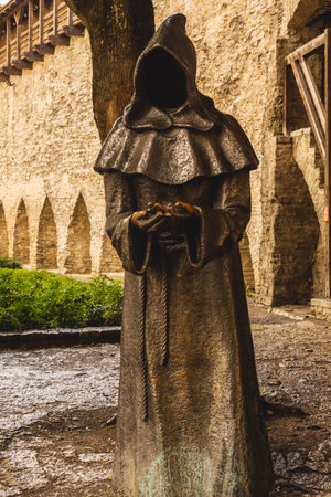 Mysterious bronze statue of a hooded monk placed in the historic Danish King's Garden of Tallinn, Estonia, with medieval architecture in the background.の写真素材