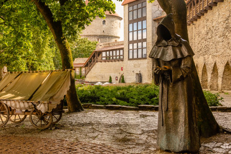 Monk statue with medieval towers, stone walls and a wooden cart in Danish Kingâs Garden, Tallinn, Estonia, captured on a rainy day, evoking historic charm.の写真素材