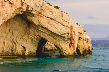 A stunning natural rock arch along the Blue Caves of Zakynthos, Greece, carved by the sea into limestone cliffs and bathed in warm afternoon light over turquoise waters.の写真素材