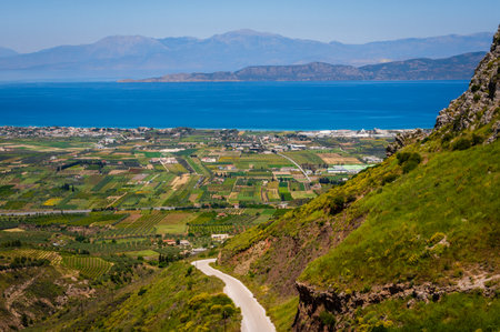 Panoramic view from Acrocorinth shows winding road, cultivated land, green fields and the calm blue Corinthian Gulf in the distance under a clear summer sky.の写真素材